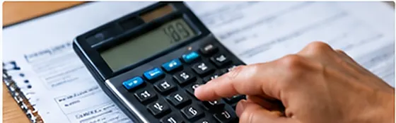 A person's hand using a calculator next to insurance paperwork